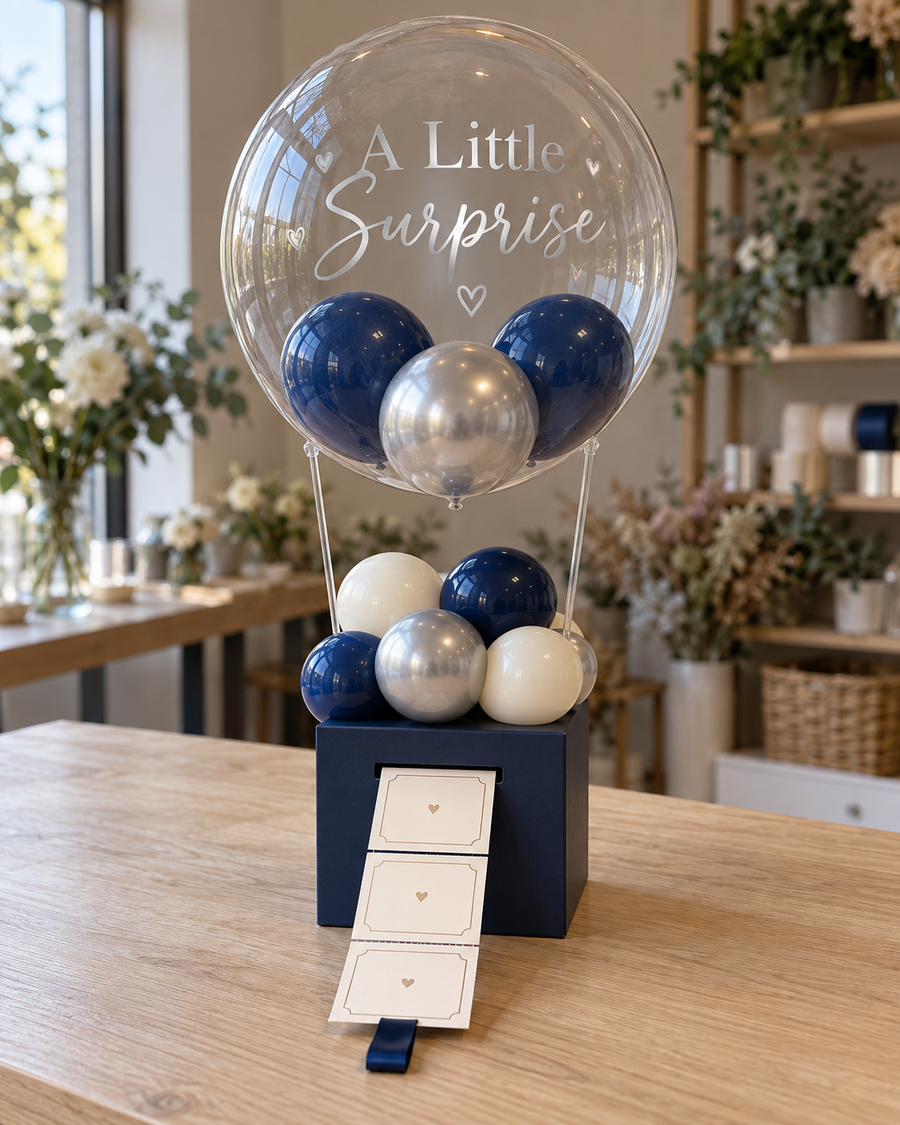 Gift studio original concept 20261009: The Little Reveal Box. A personalised bubble above a box with a pull-out strip for notes, photos or vouchers. The pictured cards illustrate the mechanism. AI concept; construction subject to prototype.